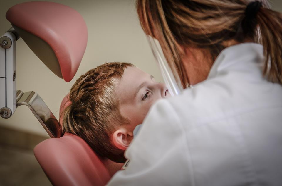 Odontóloga con mascarilla atendiendo a un niño recostado en el sillón dental